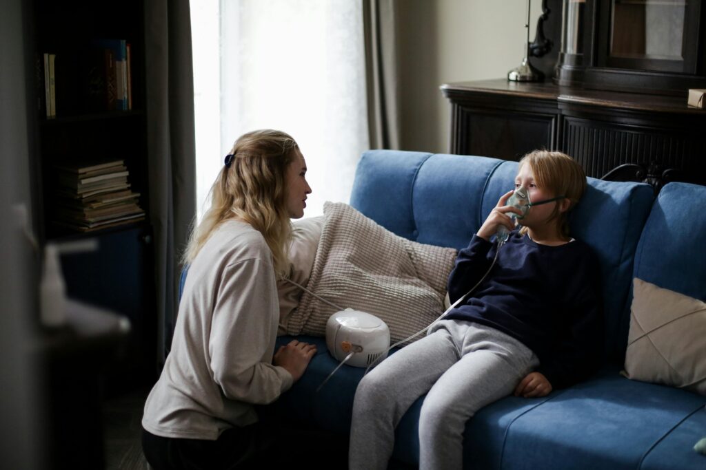 A mother assists her sick child using a nebulizer at home, providing comfort and care.