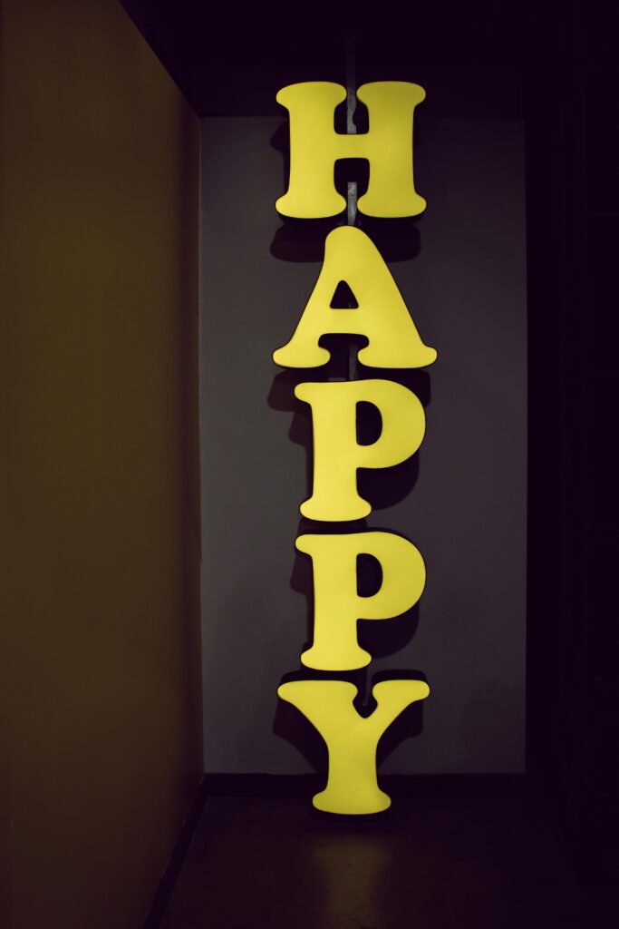 pexels-photo-1751279-1751279 Illuminated yellow 'HAPPY' sign displayed vertically in a dimly lit hallway setting, evoking a playful mood.